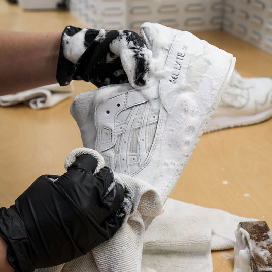 Nærbilde av vask av hvite joggesko med rensemiddel.