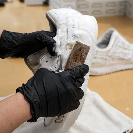 Bilde som viser skrubbing av hvite joggesko med en skobørste og rensemiddel.