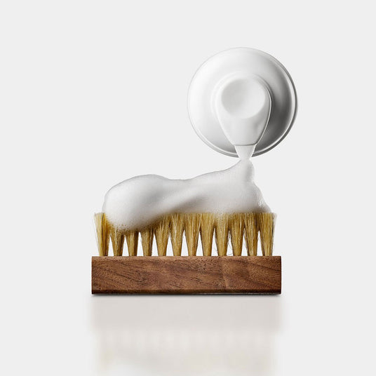 Detaljbilde som viser påføring av renseskum fra en beholder på skobørste.