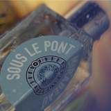 Nærbilde av glassflaske med blågrønn etikett for Eau de Parfum Sous le Pont Mirabeau